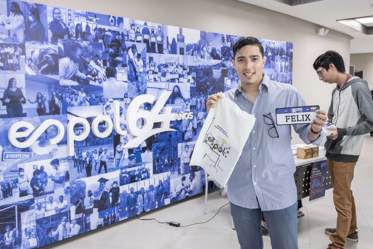 Bootcamper con su credencial frente al mural de los 64 años de ESPOL